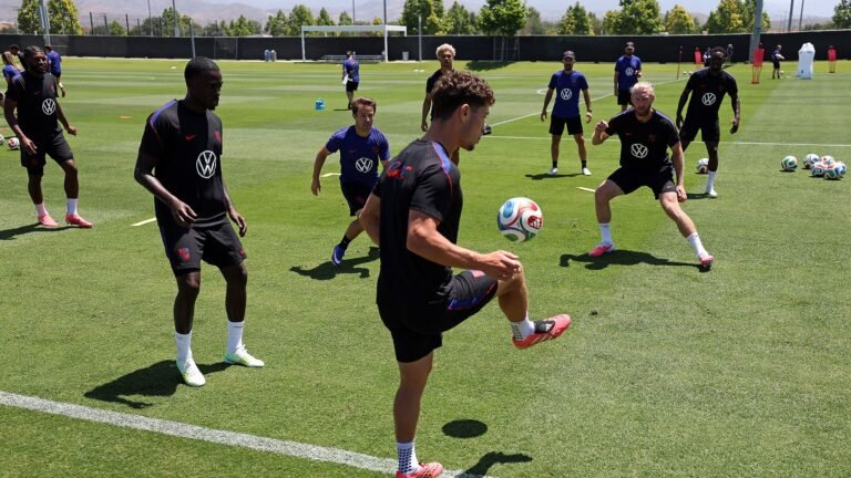 A series of men in uniforms juggle soccer balls on a green turf.