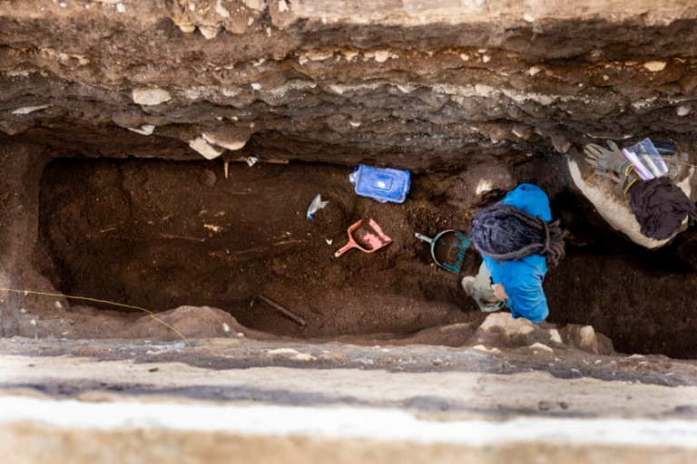 a person in a blue jacket excavates an ancient grave in a deep trench