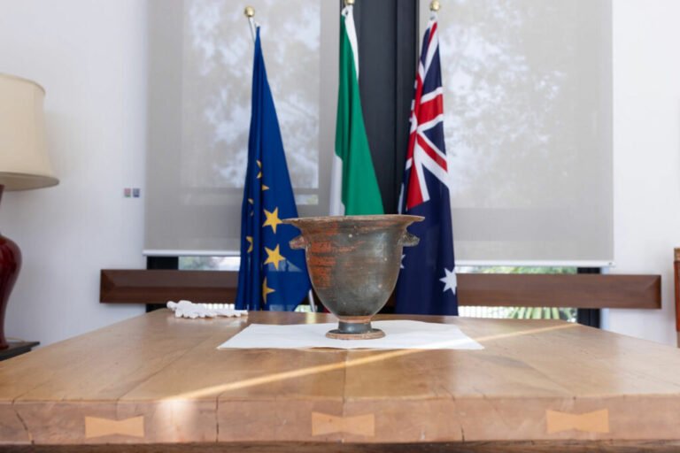 Ancient Italian bell crater sitting on a table at the Embassy of Italy in Australia, with the countries' flags in the background
